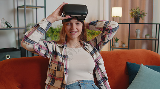 青年妇女在家里使用虚拟现实头戴眼镜 享受空中手举手的视频概念以及沙发女孩风镜技术游戏休息房子客厅公寓虚拟现实图片