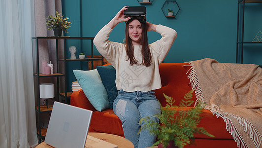 青年妇女在家里使用虚拟现实头戴眼镜 享受空中手举手的视频概念以及技术自由职业者公寓创新学习客厅青少年休息娱乐房子图片