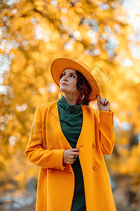 美丽的女人在秋天到户外散步 她身穿黄色外套 黄色帽子和绿色连衣裙 享受秋天天气的少妇 秋季内容头发叶子幸福日落季节女士公园快乐树图片