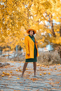 美丽的女人在秋天到户外散步 她身穿黄色外套 黄色帽子和绿色连衣裙 享受秋天天气的少妇 秋季内容叶子女士冒充毛衣围巾季节微笑头发快图片
