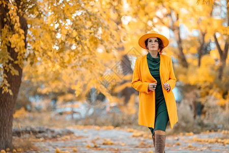 美丽的女人在秋天到户外散步 她身穿黄色外套 黄色帽子和绿色连衣裙 享受秋天天气的少妇 秋季内容青年女性幸福微笑女士日落快乐毛衣落图片