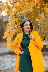 美丽的女人在秋天到户外散步 她穿着一件黄色外套和一条绿色连衣裙 享受秋天天气的少妇 秋天的内容树叶冒充女性微笑围巾毛衣公园幸福晴图片