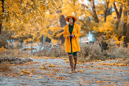 美丽的女人在秋天到户外散步 她身穿黄色外套 黄色帽子和绿色连衣裙 享受秋天天气的少妇 秋季内容树叶围巾头发日落季节皮肤幸福快乐毛图片