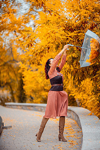 秋天公园穿着带雨伞的漂亮女孩 她把他抱在头顶上 秋叶从他身上掉出来头发天气树叶成人乐趣下雨街道黑发女性橙子图片