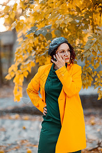 美丽的女人在秋天到户外散步 她穿着一件黄色外套和一条绿色连衣裙 享受秋天天气的少妇 秋天的内容公园青年微笑喜悦落叶女士皮肤围巾帽图片