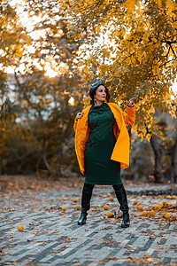 美丽的女人在秋天到户外散步 她穿着一件黄色外套和一条绿色连衣裙 享受秋天天气的少妇 秋天的内容女士女性微笑青年幸福围巾季节公园落图片