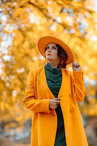 美丽的女人在秋天到户外散步 她身穿黄色外套 黄色帽子和绿色连衣裙 享受秋天天气的少妇 秋季内容公园皮肤女性围巾毛衣青年微笑乐趣日图片