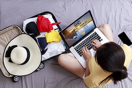 顶视图亚洲快乐女人旅行计划通过笔记本电脑预订酒店在家里的床上 带旅行包的女性使用笔记本电脑上网预订酒店 假期暑假概念游客电商手提图片