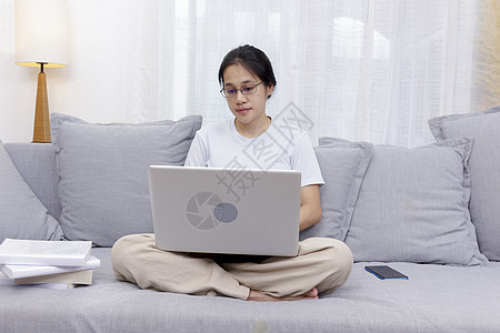 微笑的女人坐在家里的沙发上使用笔记本电脑 坐在沙发上的女性使用笔记本电脑购物 在社交网络上在线聊天 在家工作的女性在客厅使用电脑图片
