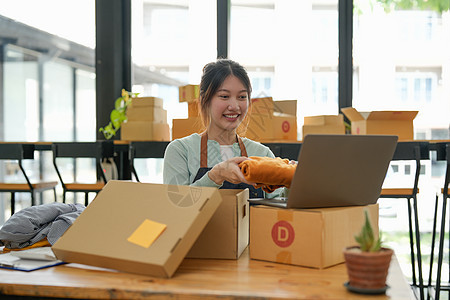 年轻的小企业主在工作场所包装纸板箱 自由职业女卖家准备产品包裹盒以交付给客户 在线销售 电子商务 运输概念电脑笔记本女士商业零售图片