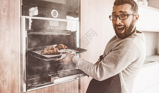 一个年轻人从烤箱里 取出牛角面包饼围裙糕点男性食物面团美食烘烤器具职业火炉图片