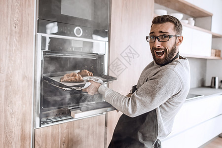一个年轻人从烤箱里 取出牛角面包饼火炉食物家庭幸福职业技术托盘围裙糕点烘烤图片