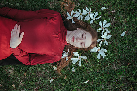 一个穿红衣服的金发女孩 躺在春天的春光中 在草丛上环绕着木兰花玉兰金发女郎公园花朵芳香疗法头发植物群眼睛裙子图片