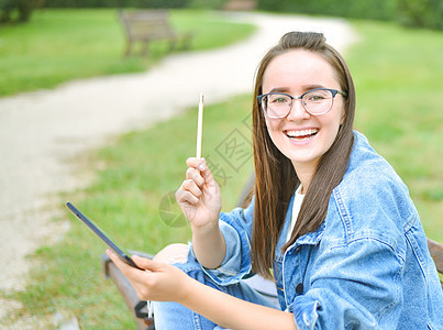 年轻美丽的女学生女孩在户外学习公园微笑学校图书长椅幸福大学女士眼镜校园图片