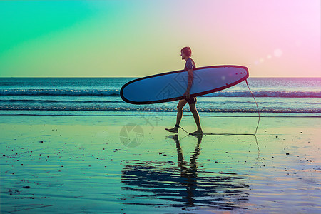 在日落时带影空间的冲浪者携带其冲浪董事会住宅的休眠活动海洋运动冲浪板天空男性乐趣太阳海岸男人日出图片