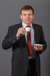 满怀自信的成熟商务人士站在灰色背景面前 喝咖啡喝一杯咖啡套装公司微笑男人人士经理领带商业男性商务图片