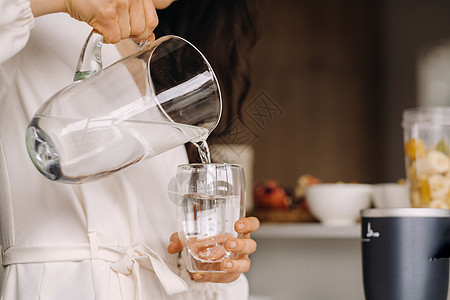 厨房里一个女孩把干净的水倒在玻璃杯上 紧紧握紧的手玻璃桌子活水液体女性化女孩饮食白色营养师茶点图片