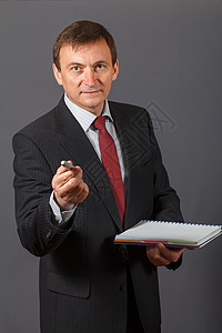 自信的成熟商务人士站在灰色背景前 拿着记号笔和笔记本男人微笑公司人士企业家套装商务领带商业男性图片