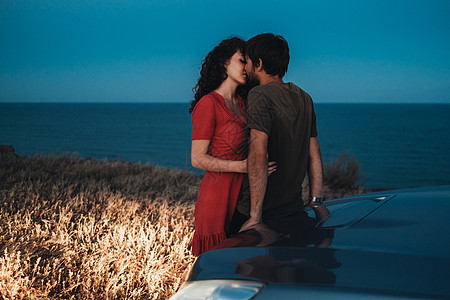 男女拥抱夜幕之夜的海岸线上 年轻夫妇男女在他们的汽车附近亲吻和拥抱背景