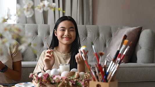 快乐的女孩画复活节鸡蛋 家里有颜色和刷子图片