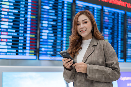 妇女在机场使用智能手机与飞行信息板的飞行信息图片
