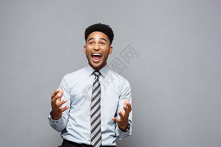 商业概念  自信的快乐年轻非裔美国人在他面前举手 在灰色背景上令人惊讶地表露出惊人的表情商务工作室工作惊喜男人男性成功员工喜悦领图片