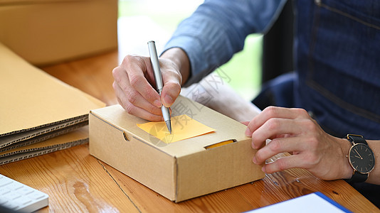 裁剪的创业企业家在准备交付产品的包裹箱时在纸箱上写地址图片