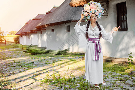 穿着白色的乌拉尼式国服和花圈的布伦特女孩 对着白小屋摆出一副花圈假期女性花束文化戏服成人裙子国家花朵房子图片