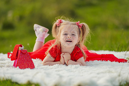 穿红裙子的女孩躺在白毯子上孩子们快乐说谎手机闲暇家庭草地喜悦工具公园图片
