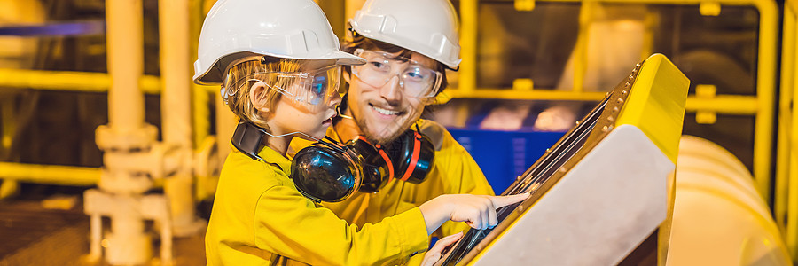 横幅 长格式 一个年轻人和一个小男孩都穿着黄色工作服 眼镜和头盔 在工业环境 石油平台或液化气厂看着屏幕图片