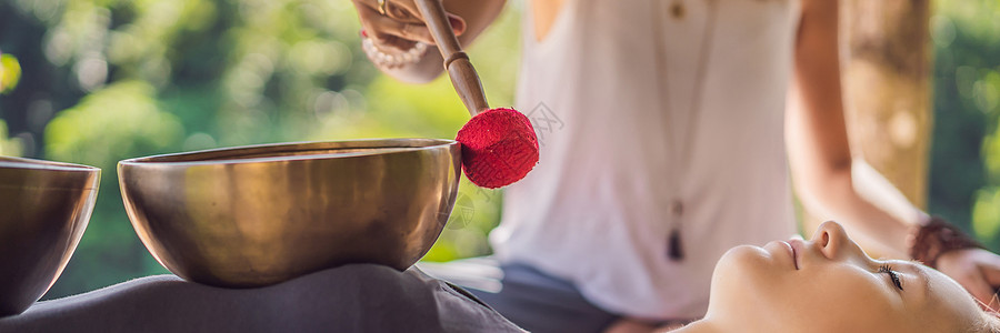 尼泊尔水疗沙龙的佛铜颂钵 年轻漂亮的女人在水疗中心对着瀑布做按摩疗法唱碗 声音疗法 娱乐 冥想 健康生活方式和身体护理概念女性康图片