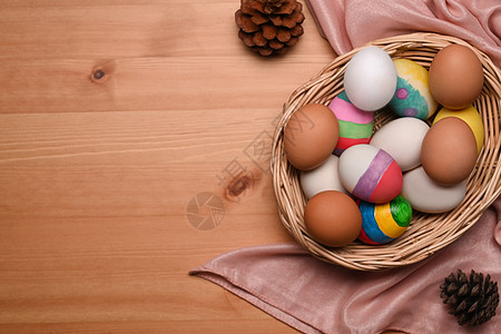 Wicker篮子里装满了油漆的复活节鸡蛋 在木制背景之上图片
