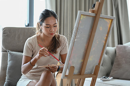 迷人的亚洲妇女在家里画画布上画画 爱好和休闲的概念图片