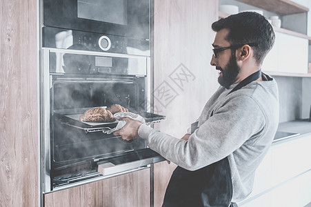 一个年轻人从烤箱里 取出牛角面包饼器具面团美食烹饪家庭幸福职业技术男人烘烤图片