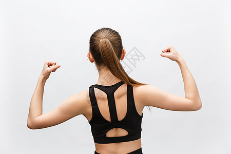 运动型女性腰部以上的镜头举起手来展示她的肌肉 对胜利充满信心 看起来坚强而独立 微笑积极 站在灰色背景下 运动理念女孩衣服工作室图片