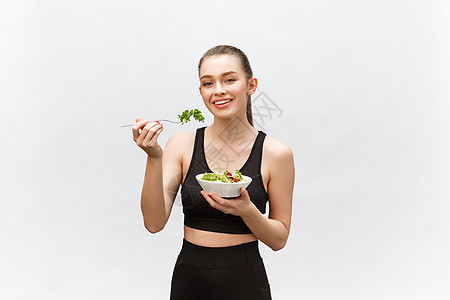 年轻漂亮的运动女郎 在白色背景下吃沙拉营养女士快乐蔬菜美食成人节食喜悦微笑食物图片