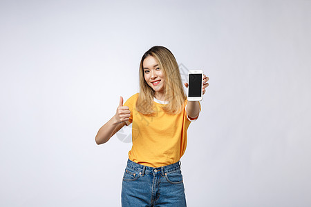 商务衬衫身穿黄衬衫的亚洲年轻女性 在白色背景上举起拇指标志 拿着手机 微笑黑发成人健康学生商业技术细胞屏幕商务女士背景
