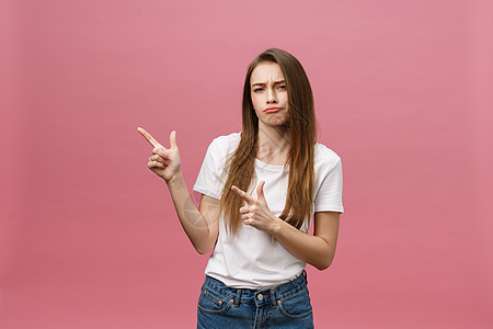 穿着白衬衫 严肃严肃的年轻女性的特写看起来压力重重 手指在粉红色背景中被隔离女士衬衫青少年惊喜相机积分女孩成人头发金发女郎图片