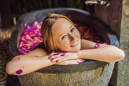 有魅力的年轻女人在沐浴着热带花卉和芳香油的花瓣 用于皮肤再生的水疗护理 Spa 沙龙的迷人女人 放松在有花瓣的浴缸的女孩 奢华液图片