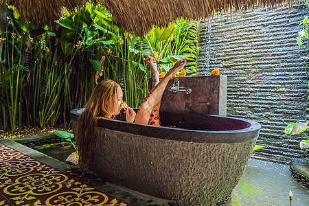 有魅力的年轻女人在沐浴着热带花卉和芳香油的花瓣 用于皮肤再生的水疗护理 Spa 沙龙的迷人女人 放松在有花瓣的浴缸的女孩 奢华身图片