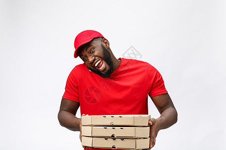 交付概念 英俊的非洲比萨饼送货员用令人震惊的面部表情与移动交谈 孤立于灰色背景手势惊喜盒子工人说话服务食物互联网技术工作图片
