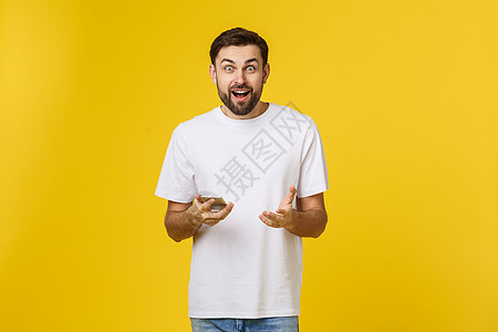朋友的好消息 穿着牛仔裤衬衫的自信英俊年轻男子在黄色背景下拿着智能手机电话细胞微笑商业技术幸福空白白色快乐短信图片