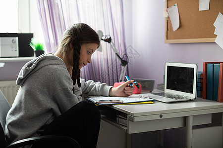 有个学生坐在课桌边做功课互联网角落任务屏幕倾斜笔记本学习远程电脑女孩图片