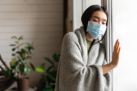 身戴着医疗面罩的生病的亚洲女孩站在窗边 渴望外出 被隔离 患19岁或感冒病心碎疾病感染发烧流感房子女性杯子毯子肺炎图片