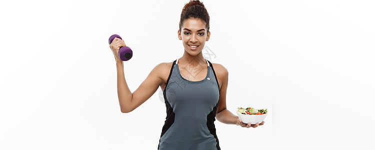 健康和健身概念美丽的运动非洲裔美国人手上拿着哑铃和新鲜沙拉节食 孤立在白色工作室背景上营养饮食沙拉重量女性早餐训练身体紫色食物图片