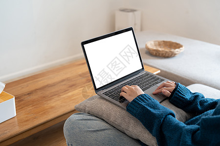 一名坐在家中沙发上用空白屏幕在笔记本电脑上工作并打字的妇女的顶级模拟图像图片