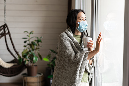 身戴医疗面罩的亚裔女孩 渴望外出 患上19岁胎儿病和在家中进行自我隔离痛苦互联网感染女性毯子流感房子窗户发烧杯子图片