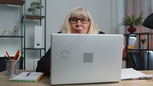 年长成熟的老年商业妇女躲在笔记本电脑后 制造笑脸 玩弄花样祖母退休训练商务金融职场办公室老人微笑工作图片