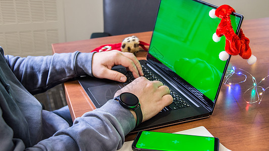 特写男人手在笔记本电脑键盘上打字 背景是空绿屏 智能手机模型和圣诞装饰 假期的概念 办公室 小样展示绿色饰品购物色度庆典屏幕互联图片