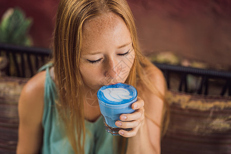 女青年在沙发上吃地中海早餐 喝特伦迪饮料 蓝拿铁热蝴蝶咖啡拿铁或蓝螺旋兰拿铁女性奶油咖啡店杯子玻璃蝴蝶女孩食物饮品动物图片